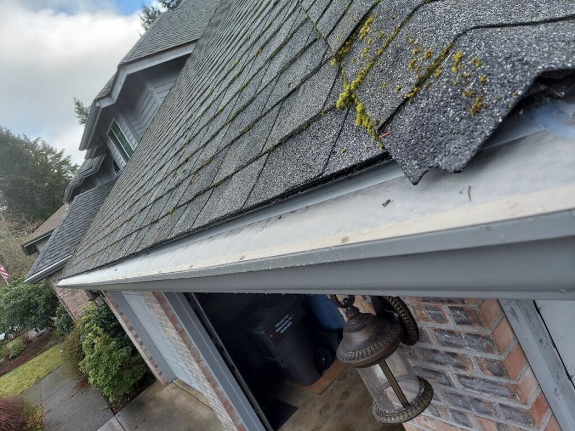 Damaged shingle and gutter section overflowing above a garage roofline